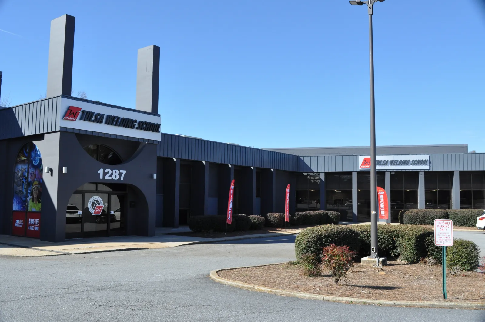 Exterior view of Tulsa Welding School building with signage, flags, and clear blue sky at 1287 address.