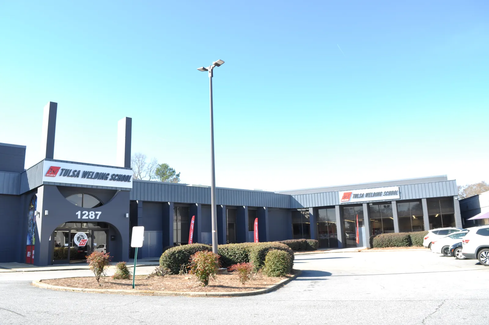 Exterior of Tulsa Welding School building with clear sky, parking lot, and landscaping in front of it.