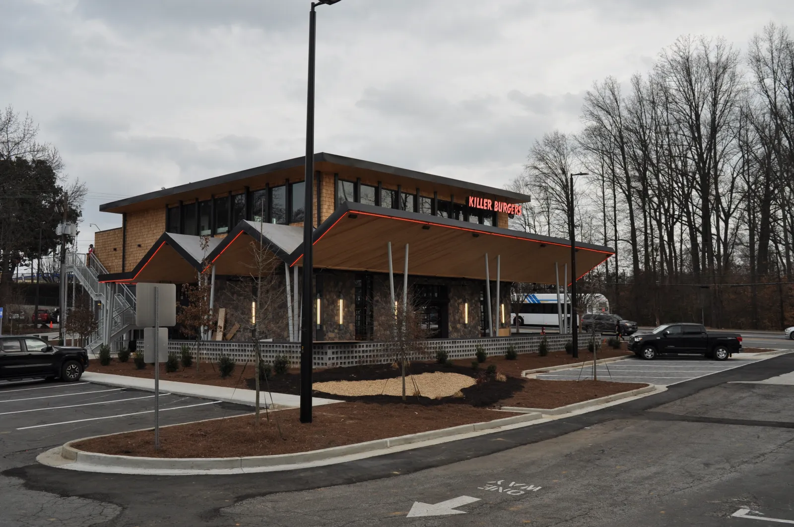 Modern Killer Burgers restaurant building with angled roof, stone exterior, and parking lot under cloudy sky