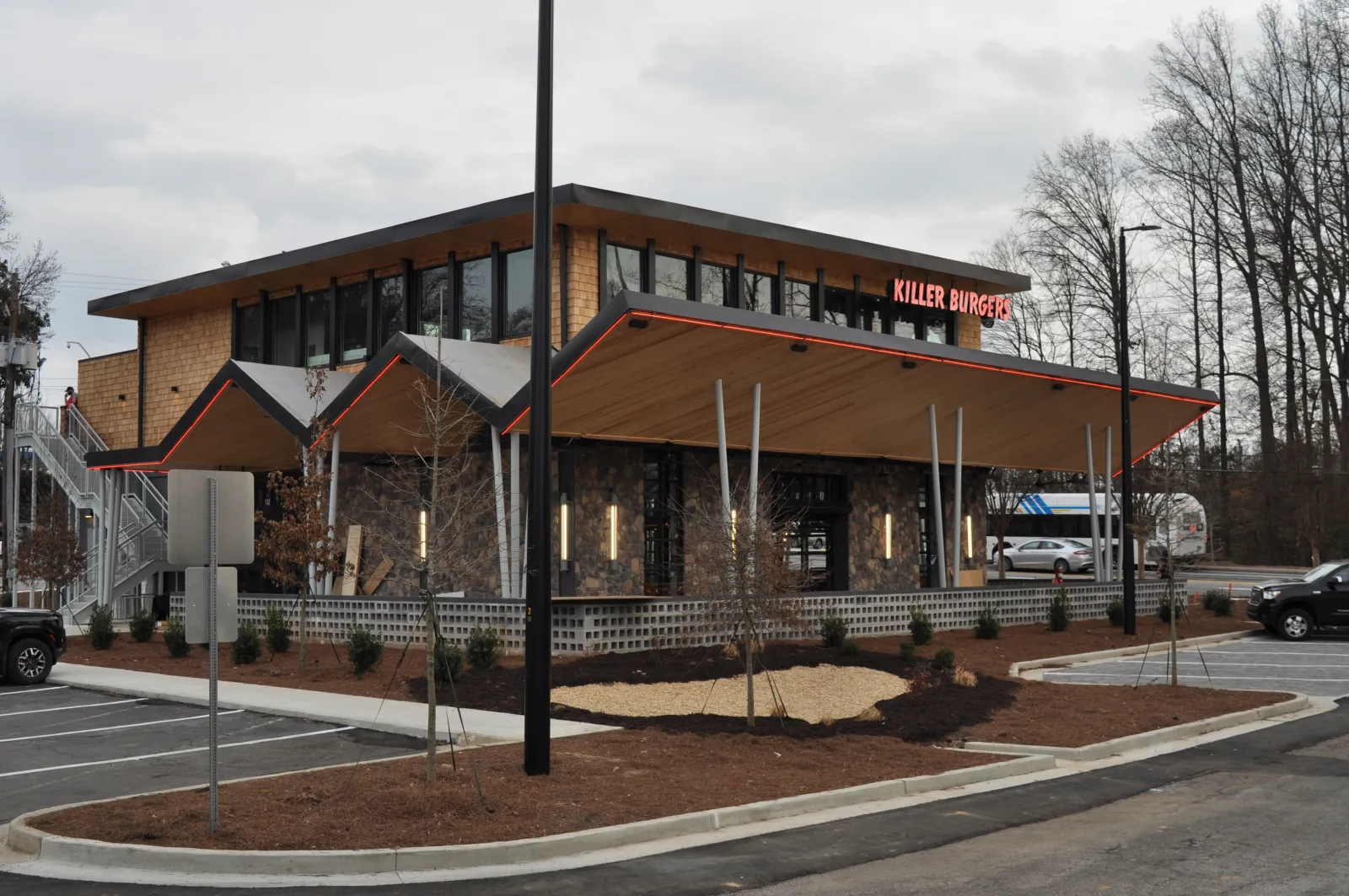 Modern Killer Burger restaurant with sharp angled roof, large windows, and parking lot on a cloudy day