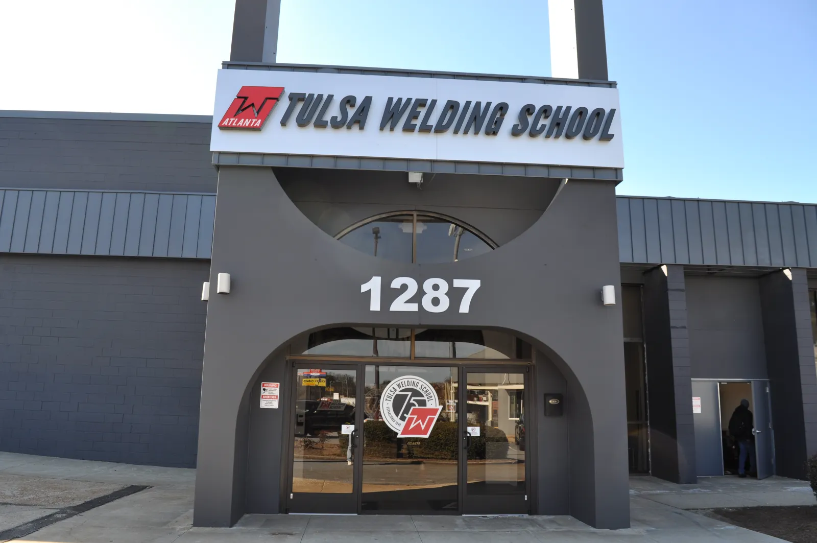 Entrance of Tulsa Welding School building with address 1287 and school logo on glass doors under clear sky.