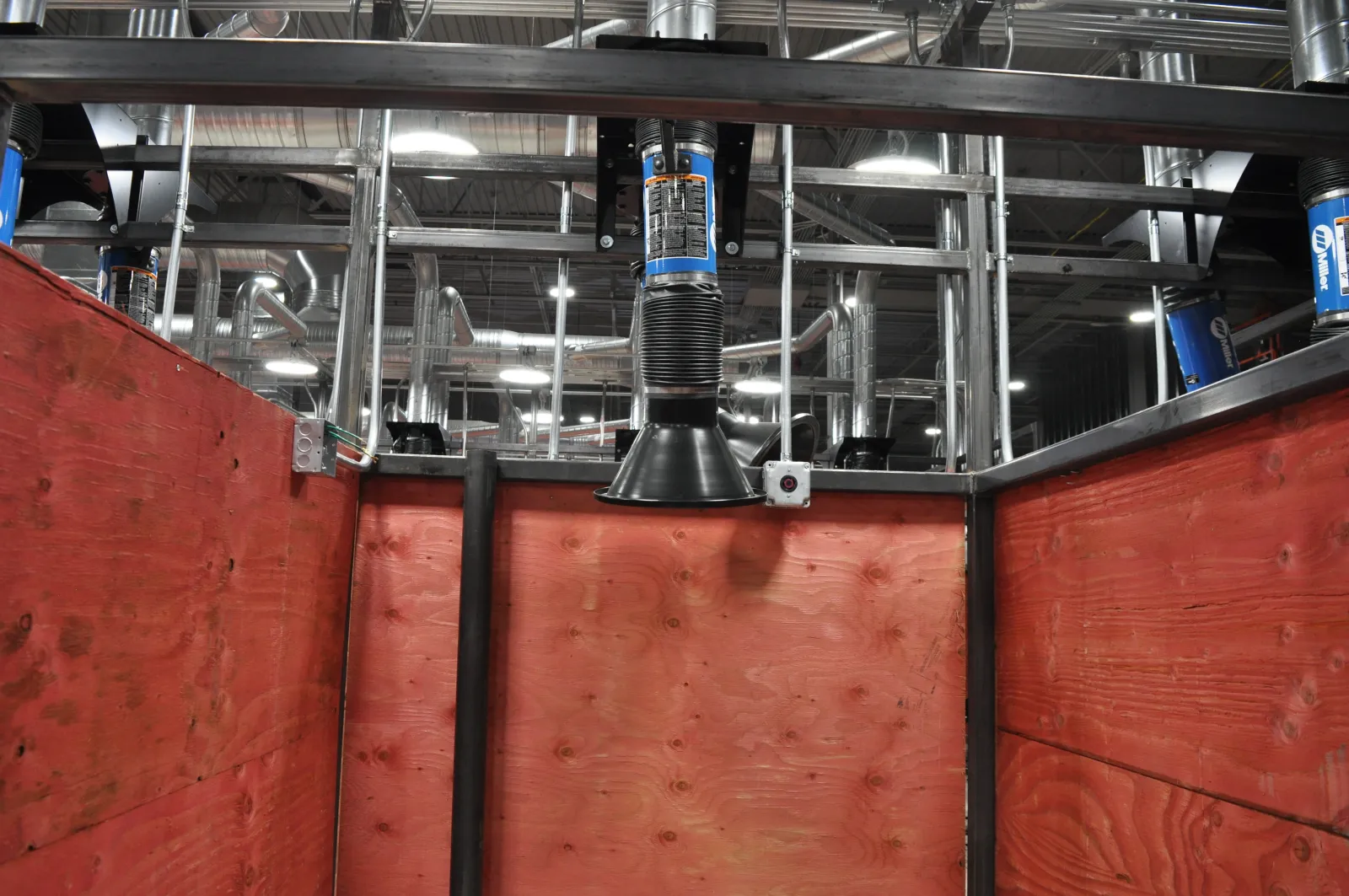 Wooden enclosure with ventilation ducting and industrial ceiling in a spacious facility.