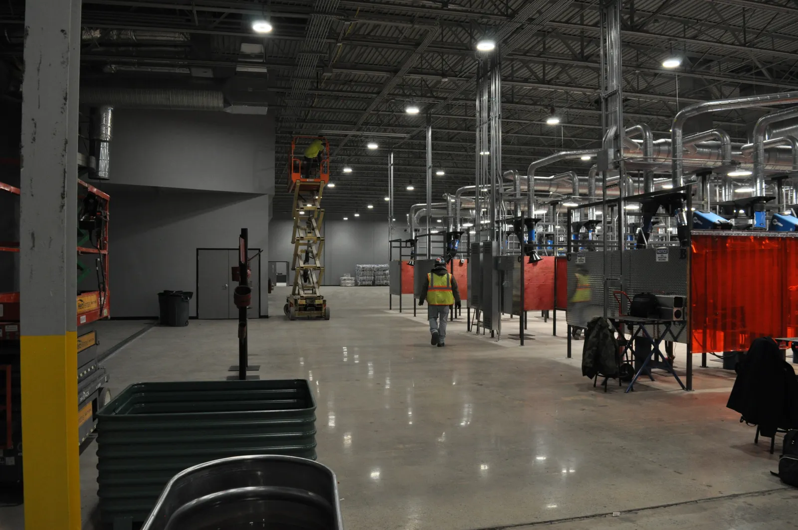 Spacious industrial workshop with welding stations, workers in safety vests, and equipment under bright ceiling lights