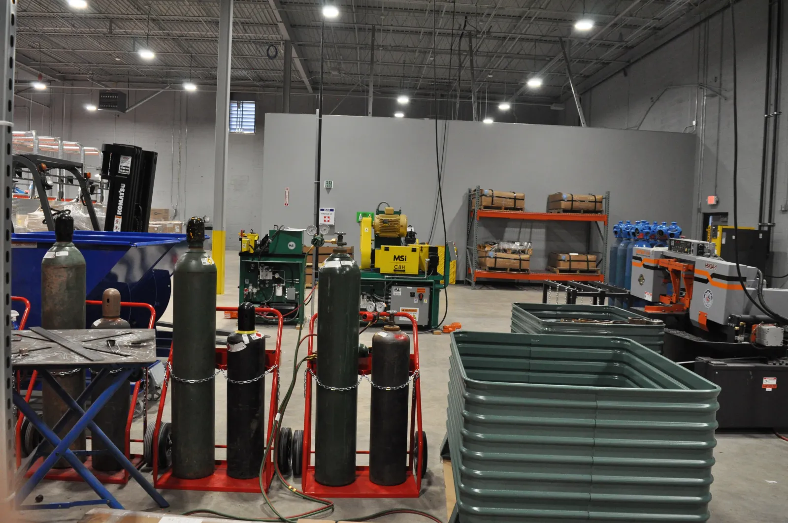 Industrial workshop with gas cylinders, machinery, metal containers, and equipment for manufacturing processes.