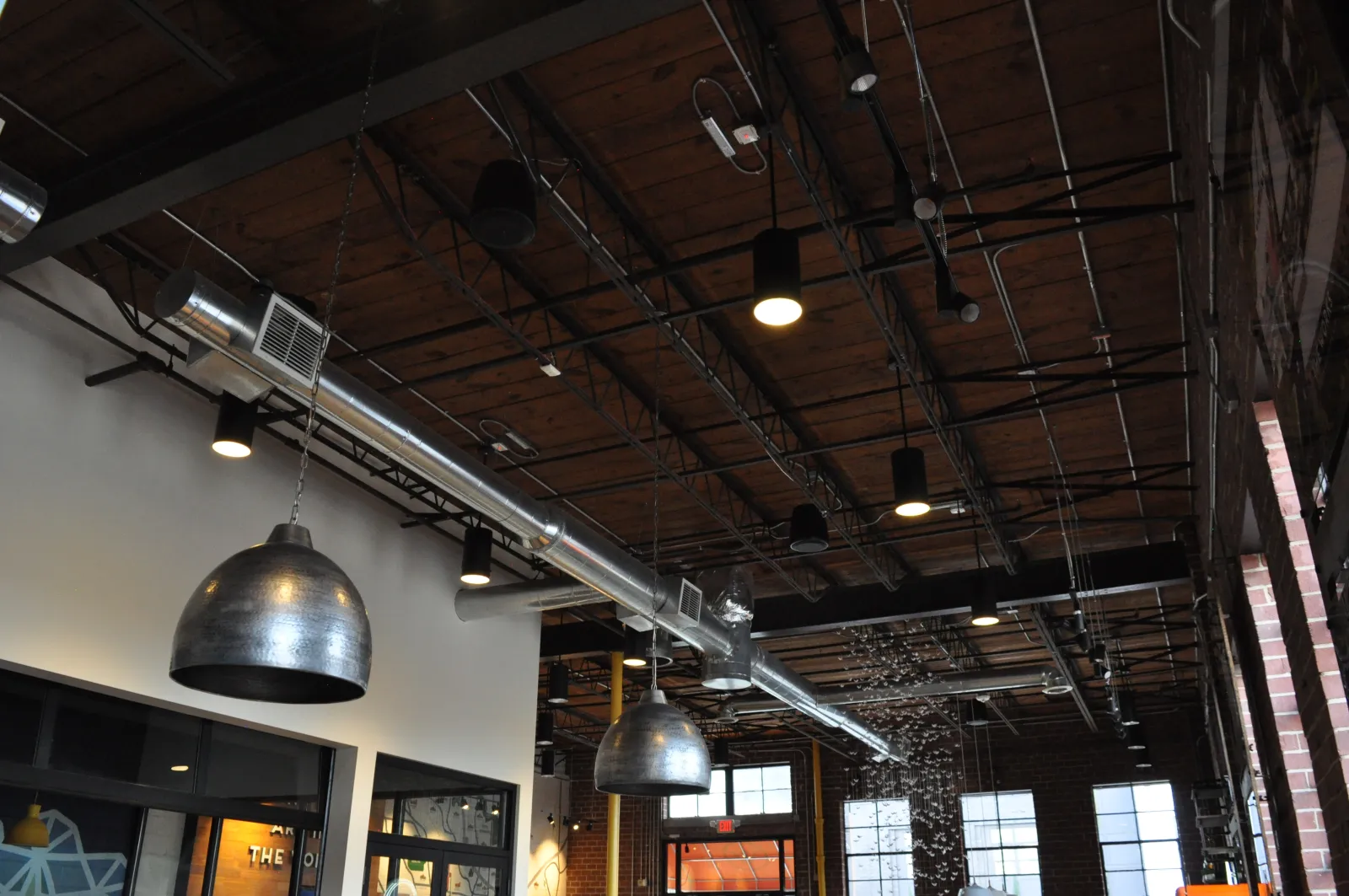 Industrial ceiling with exposed ductwork, hanging metal pendant lights, and wooden beams in a modern interior.