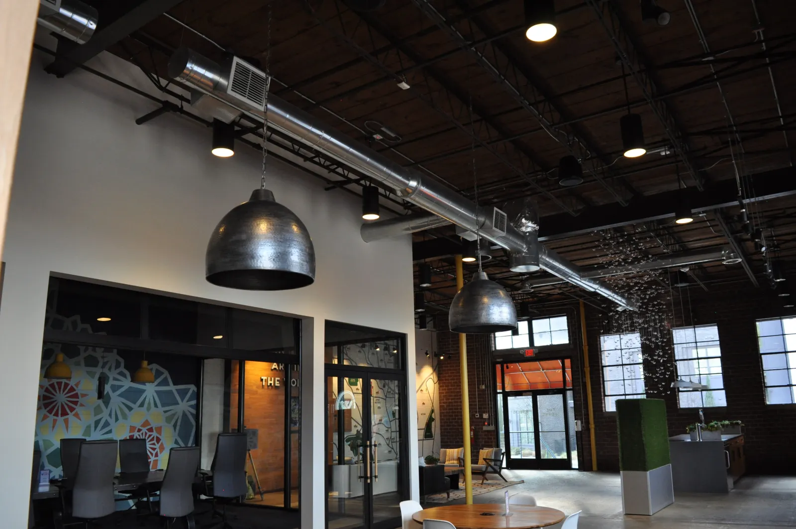 Spacious modern office interior with industrial design, exposed ductwork, pendant lights, and meeting rooms.