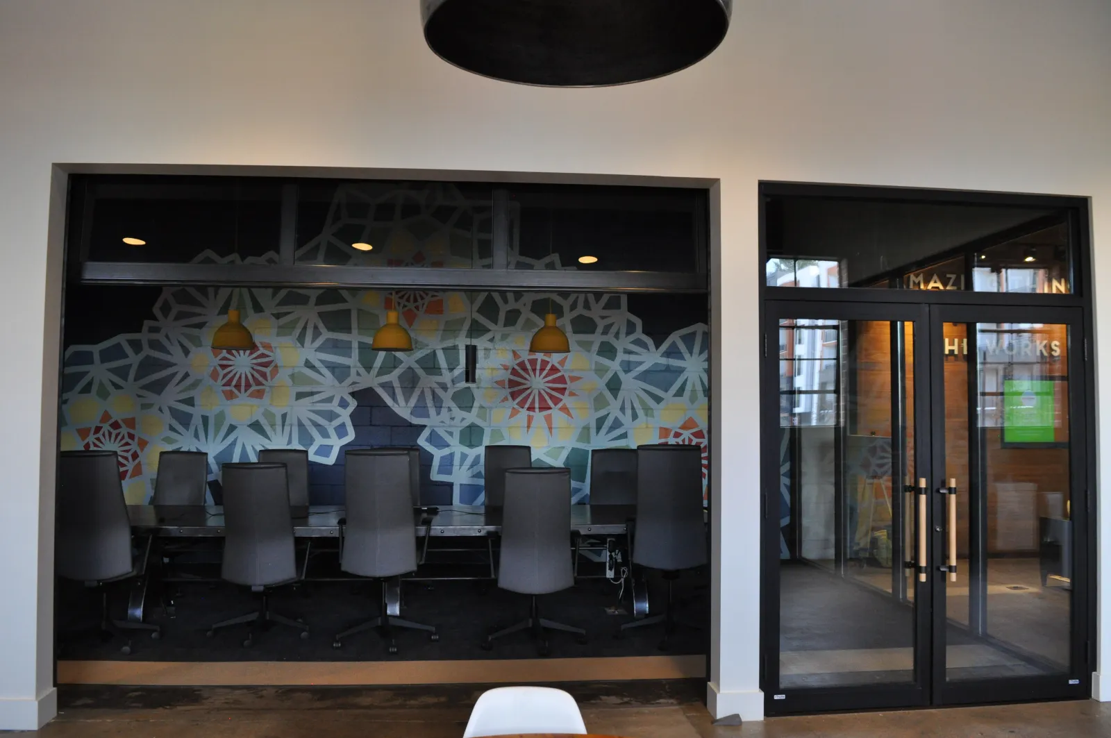 Modern office conference room with black chairs, geometric wall art, and glass entrance doors under hanging lights