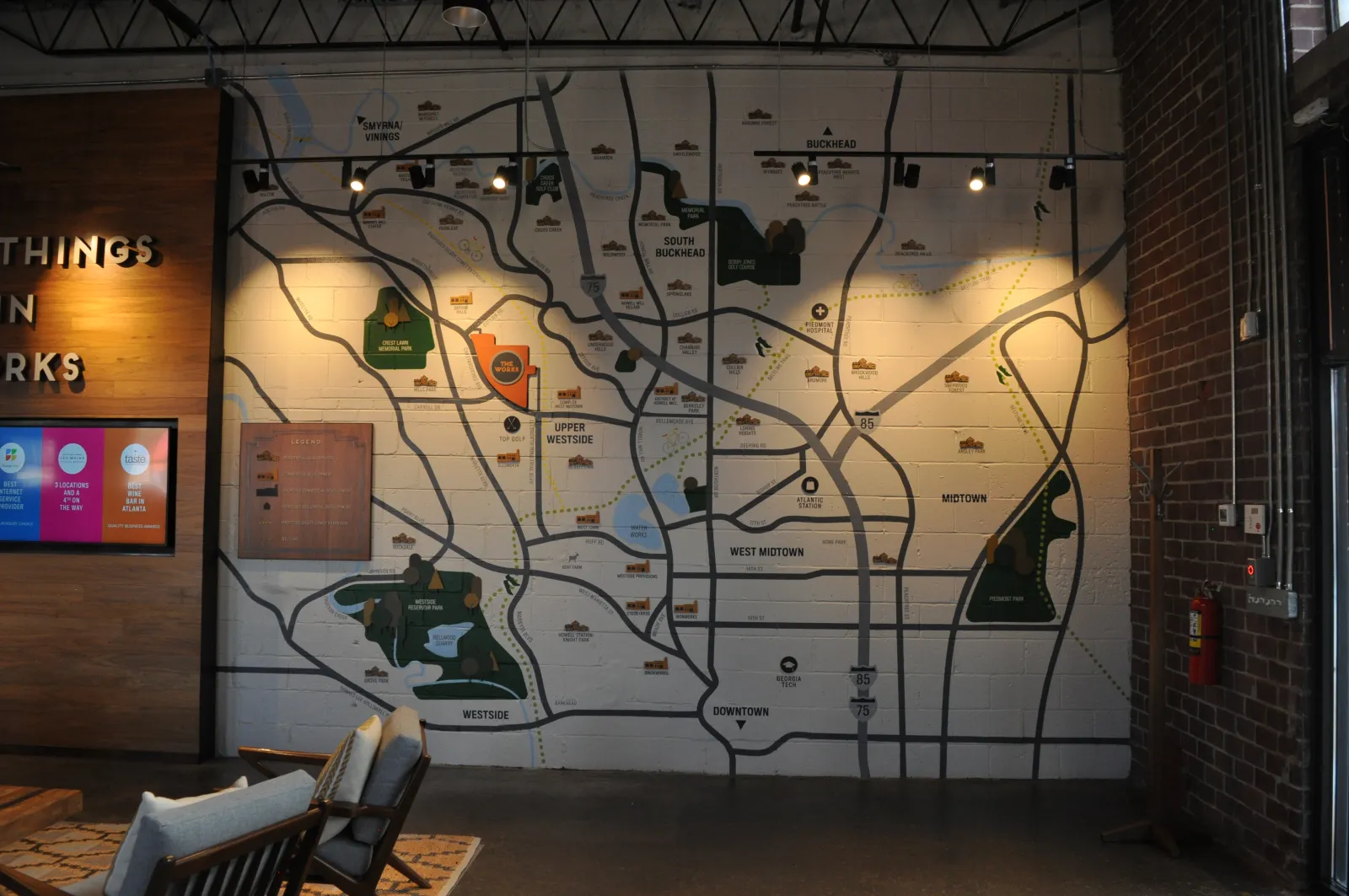 Large wall map of city neighborhoods and parks displayed in a modern indoor space with chairs and wooden decor.