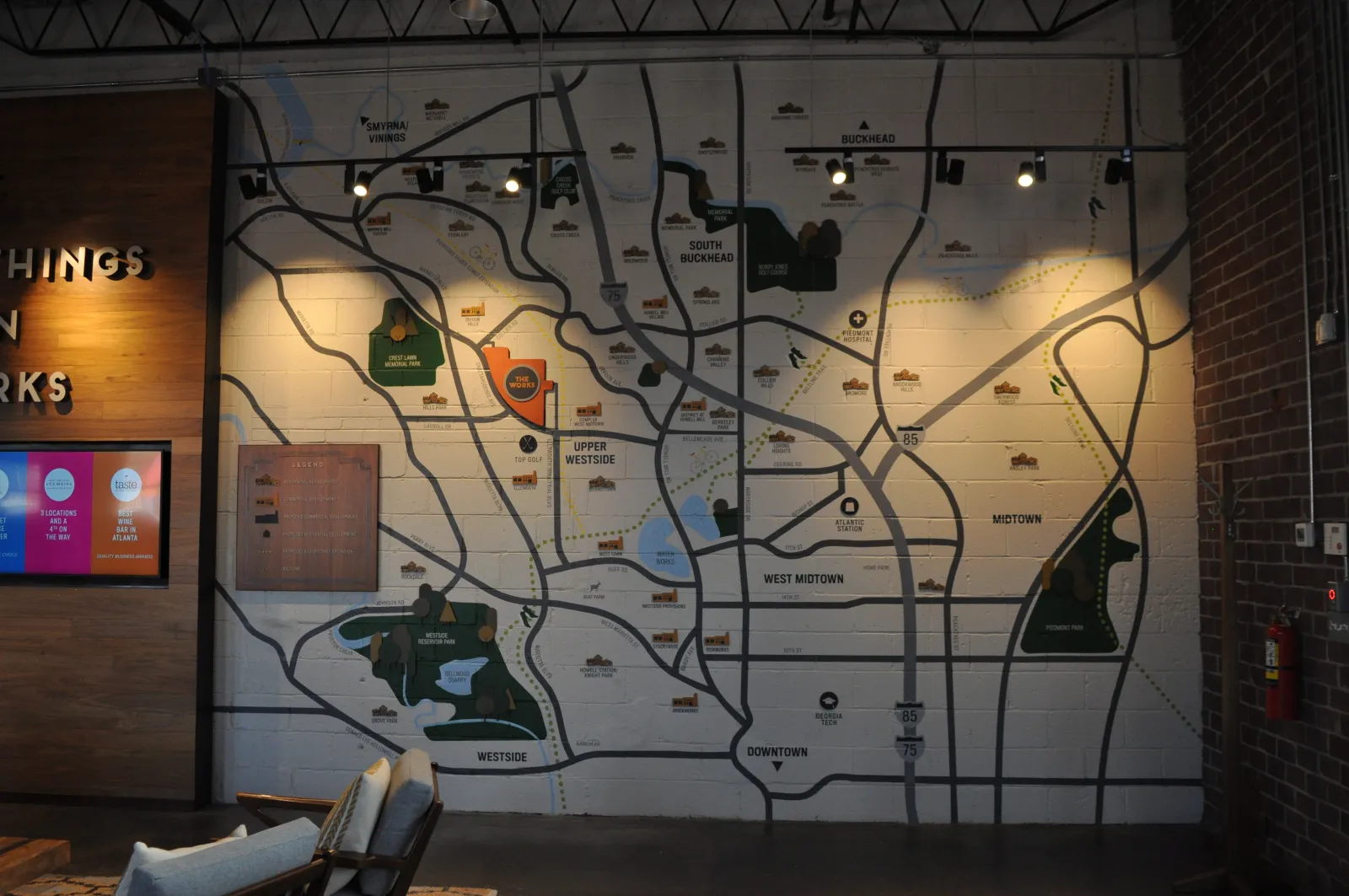 Large wall map highlighting Atlanta neighborhoods and parks with bold road lines and icons in an indoor lounge setting.