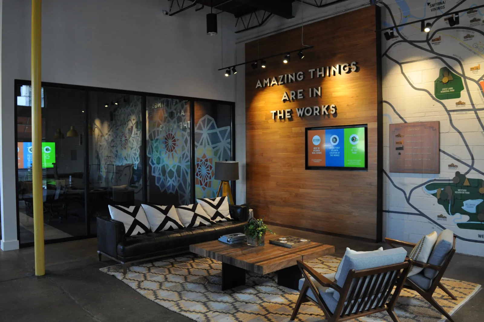 Modern office lounge with black couch, wooden table, patterned rug, wall sign reading Amazing Things Are In The Works