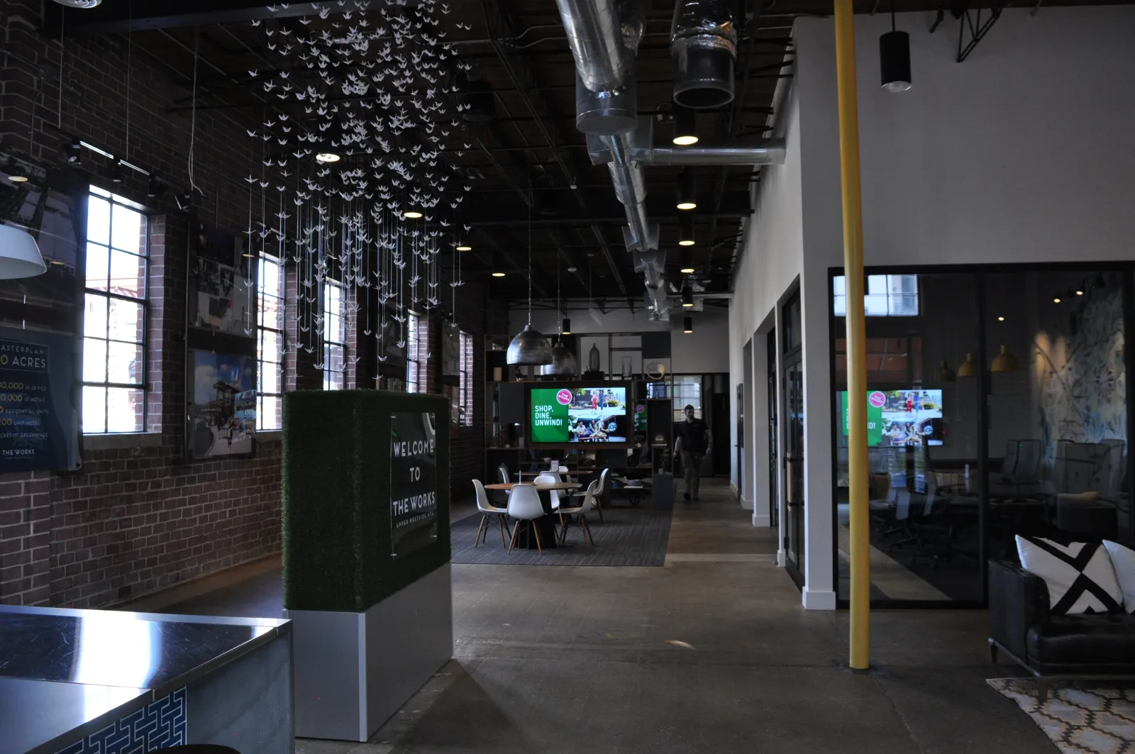 Modern industrial office space with brick walls, large windows, hanging bird decorations, and a meeting area.