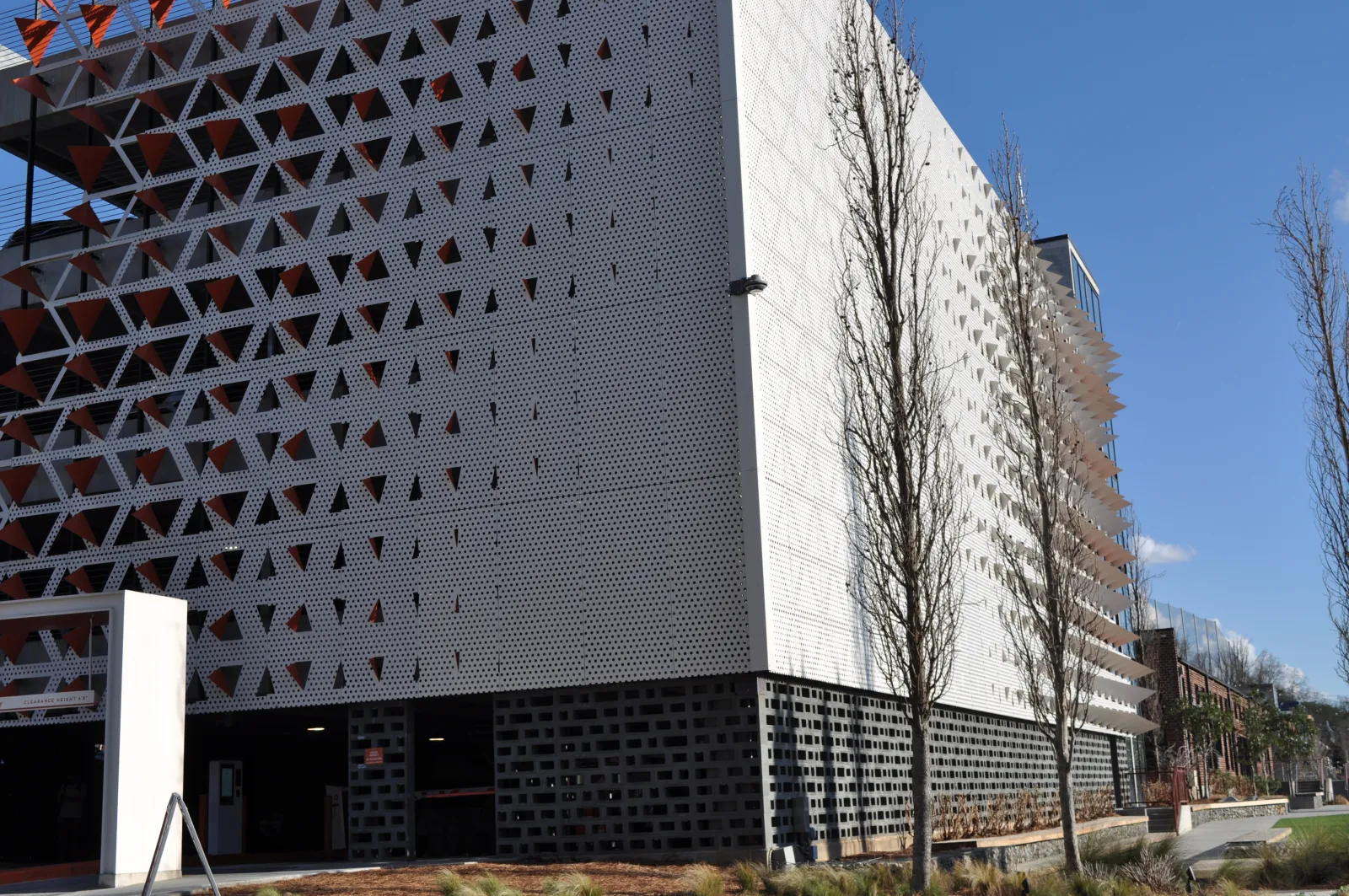 Modern building with perforated geometric facade panels and leafless trees under clear blue sky.