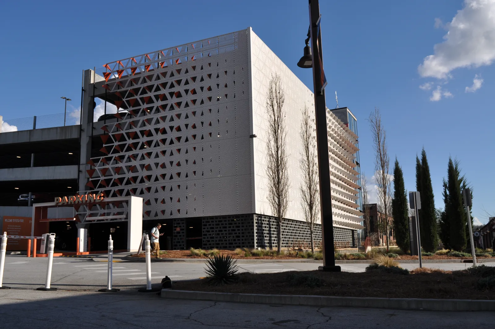 Modern parking garage with geometric facade, trees, and blue sky in an urban setting on a sunny day