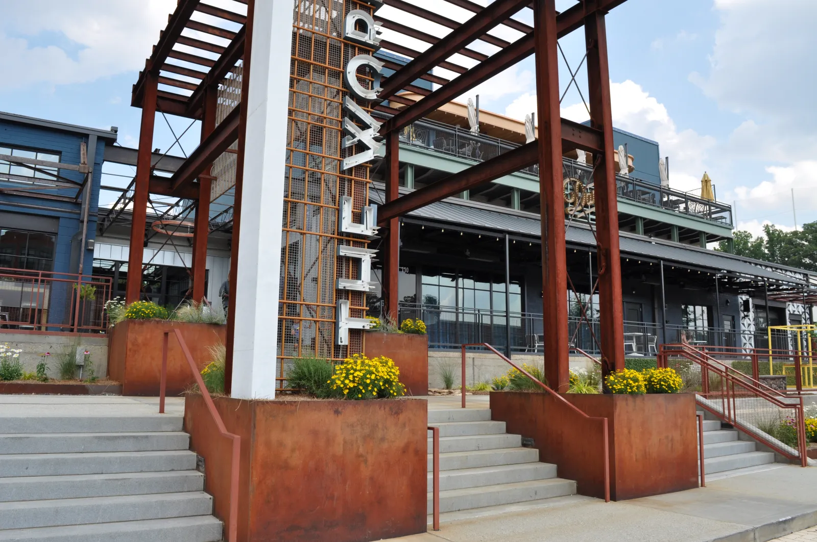 Rustic modern industrial building entrance with large steel beams and yellow flowers on sunny day