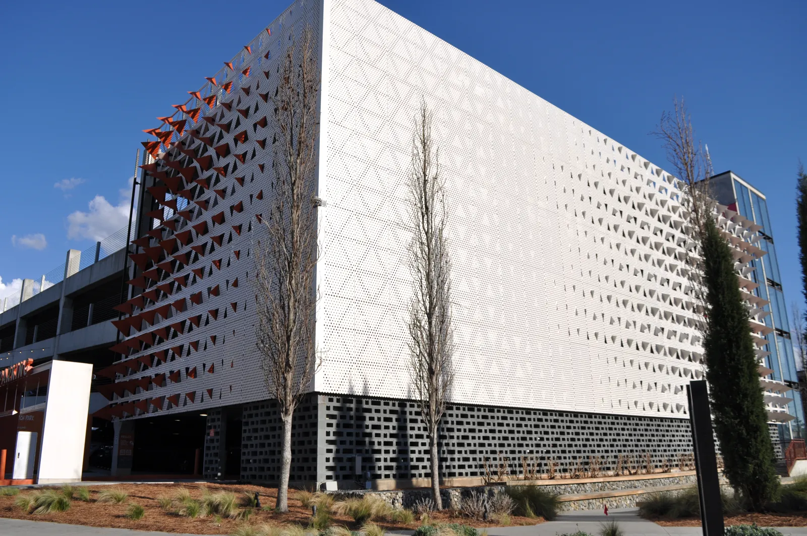 Modern building with geometric patterned white facade and sparse trees under clear blue sky