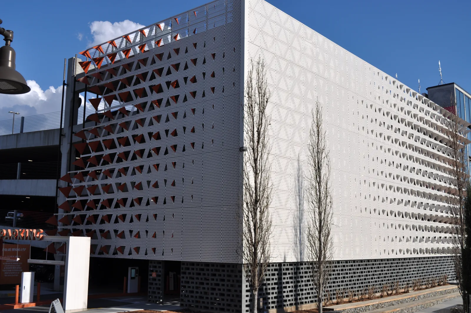Modern parking garage with perforated metal facade featuring triangular patterns under a clear blue sky.