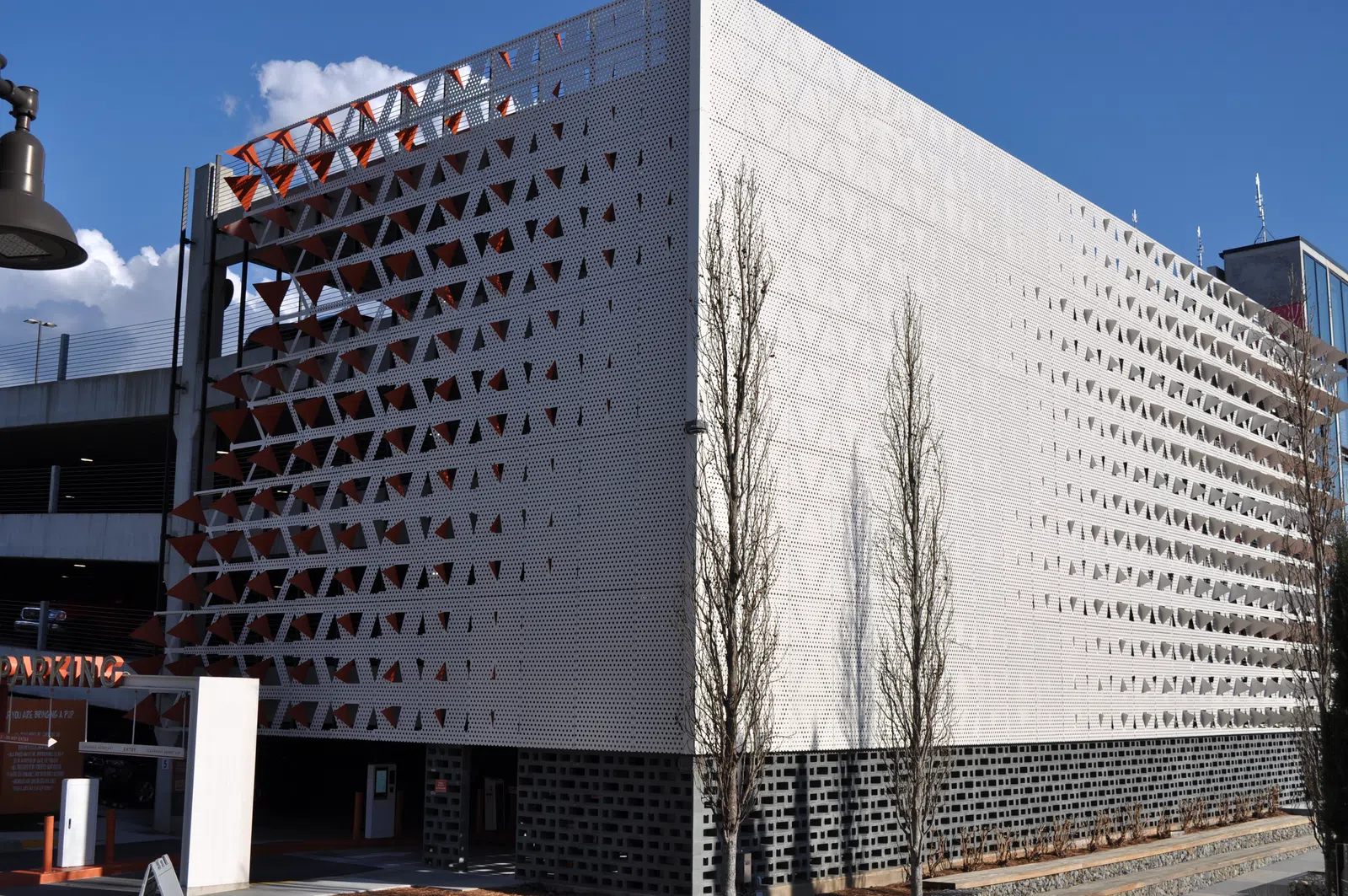 Modern parking garage with white perforated metal facade and geometric triangular patterns under clear blue sky