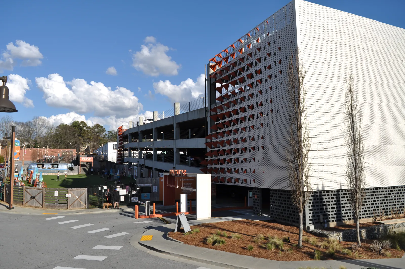 Modern multi-level parking garage next to a fenced green space park under a blue sky with clouds.