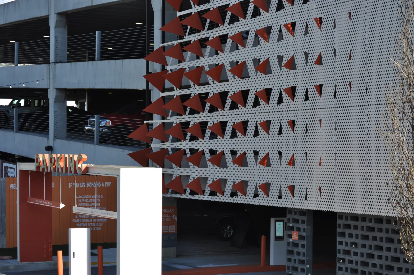 Modern parking garage entrance with orange triangular accents and visible parked cars inside the structure