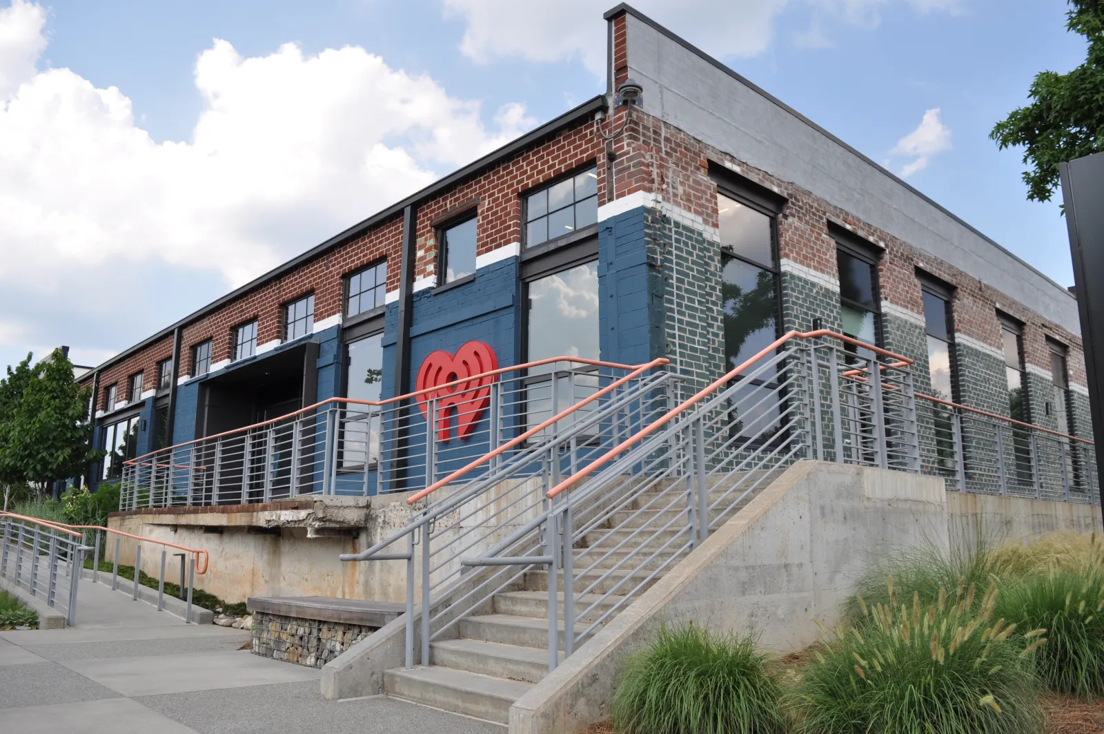 Modern brick building with large windows and iHeartRadio logo under blue sky with clouds