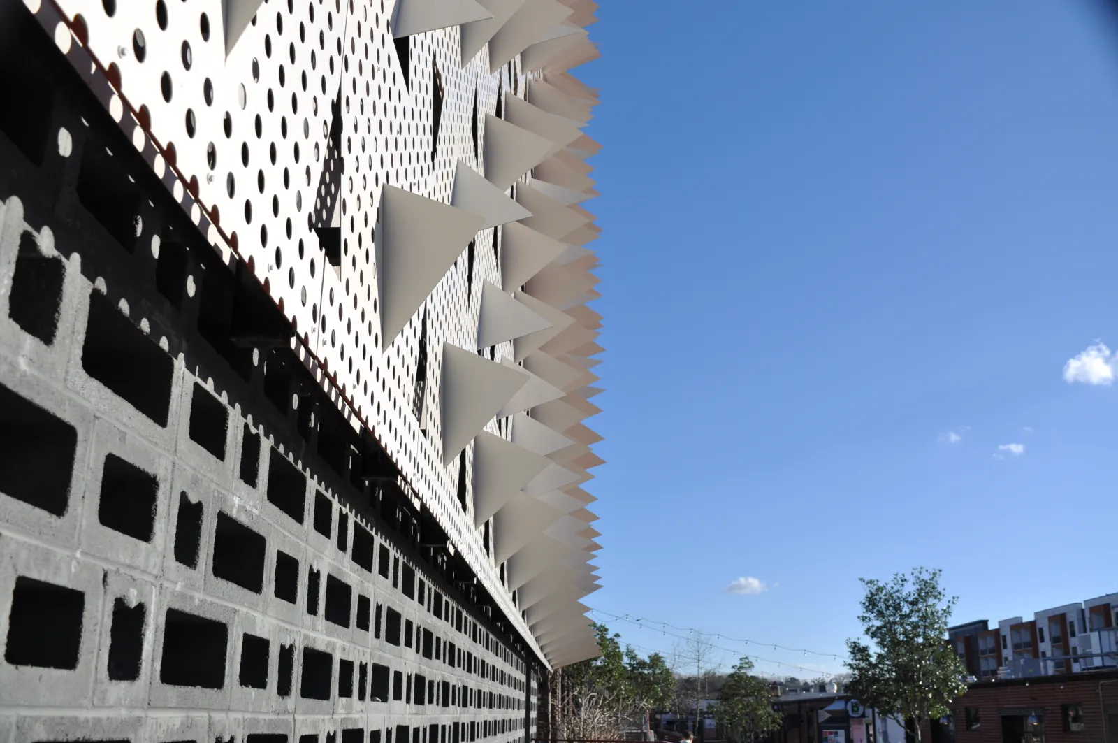 Modern building facade with geometric patterns and protruding white triangular shapes under a clear blue sky.