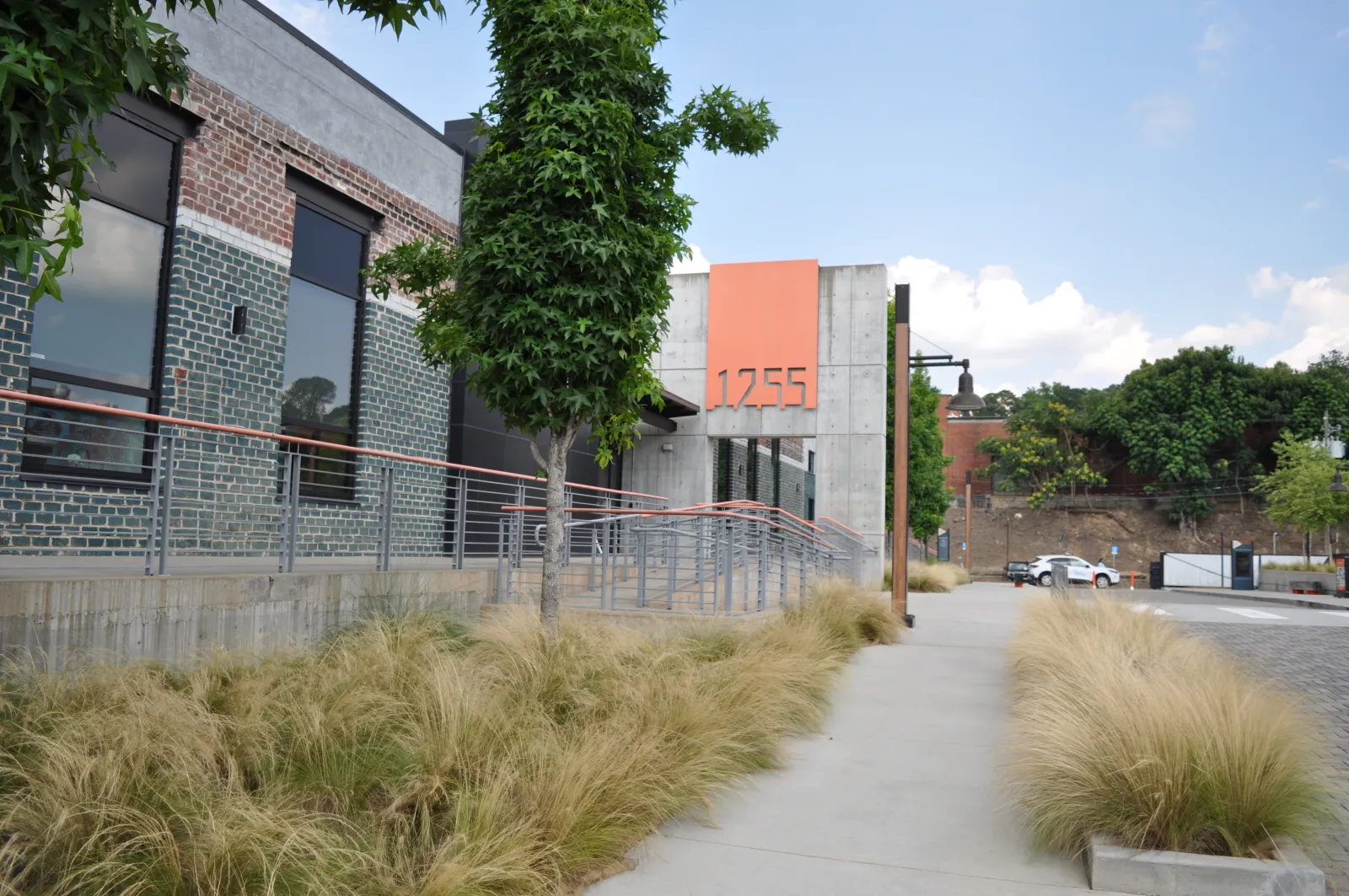 Modern commercial building with large windows, tall grass landscaping, and number 1755 on orange panel.