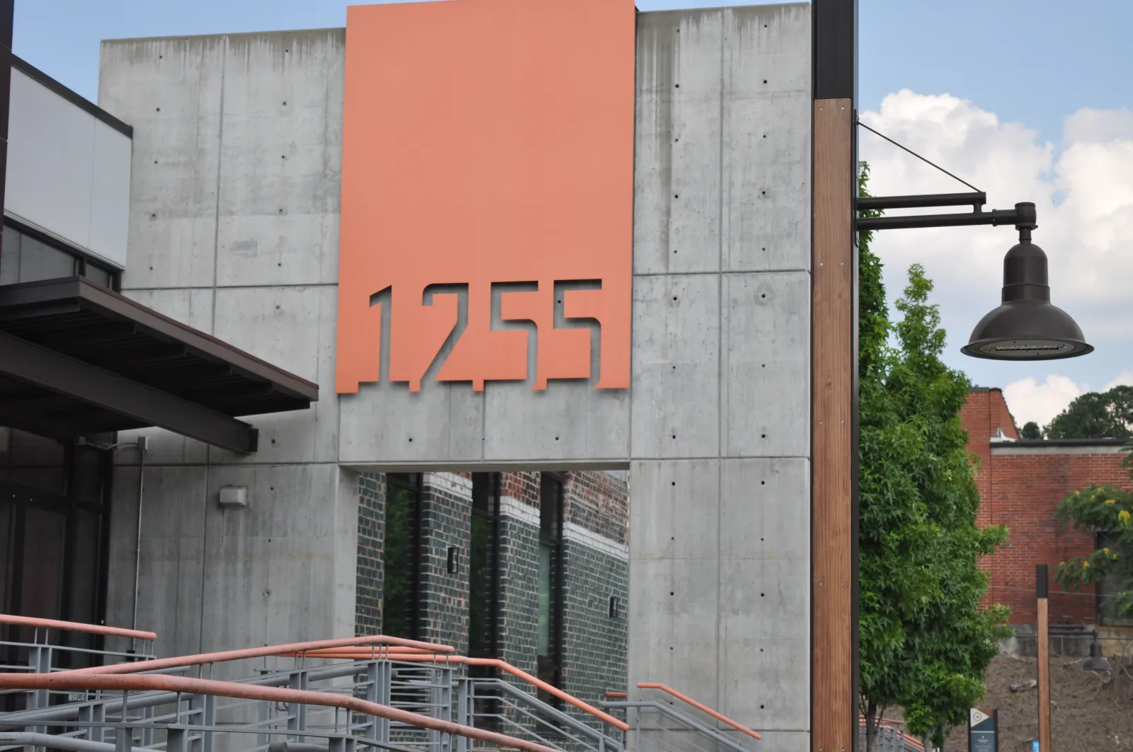Modern building facade with large orange address number 1255 on gray concrete wall near a staircase and street lamp.