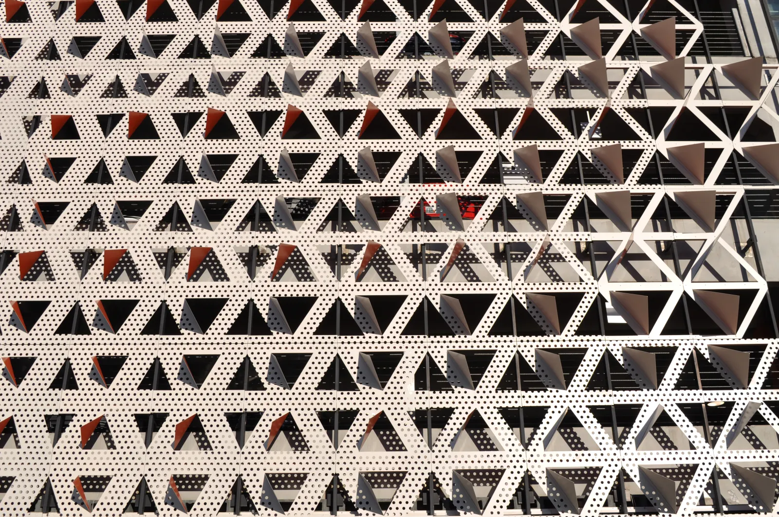 Facade of a modern building with repeating perforated white triangular patterns creating geometric shadows.