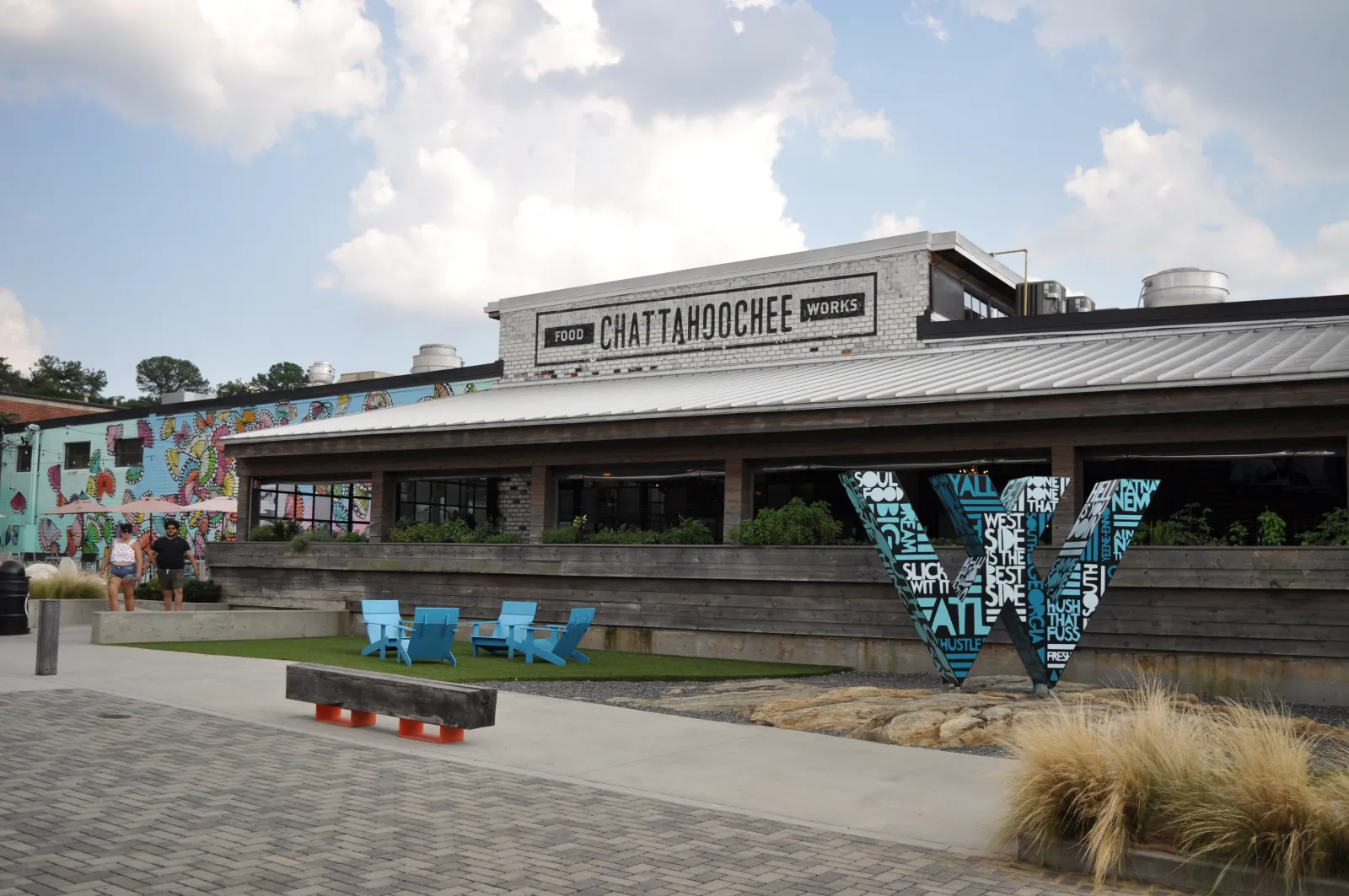 Outdoor view of Chattahoochee Works food hall with mural, blue chairs, and large decorative letter W