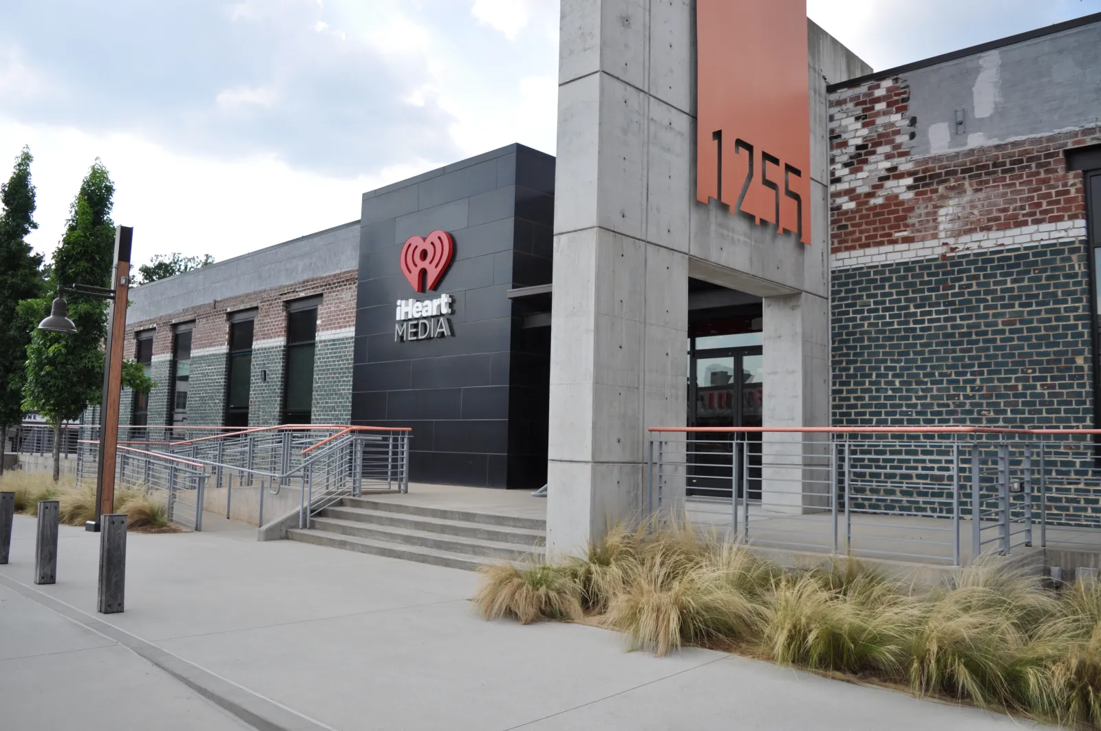 Modern iHeart Media building entrance with concrete pillars and black and brick exterior at 1255 address.