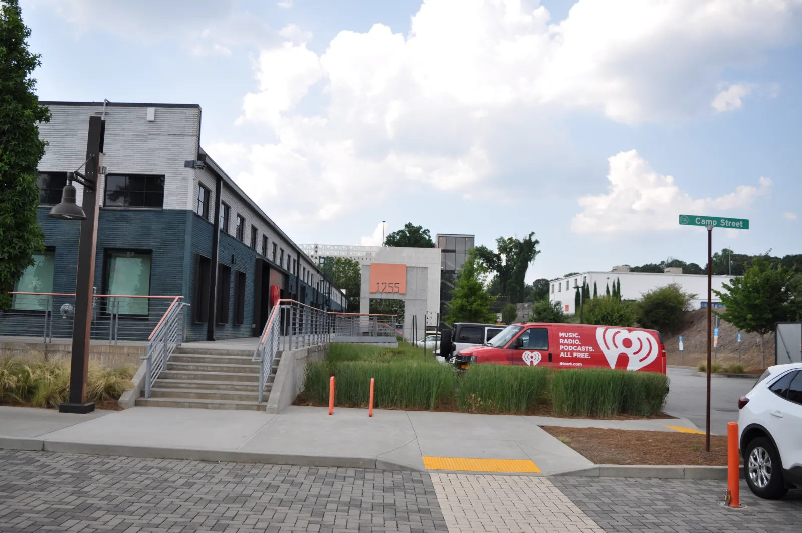 Modern commercial building with gray facade, a red and white iHeartRadio van parked near Camp Street on a sunny day.