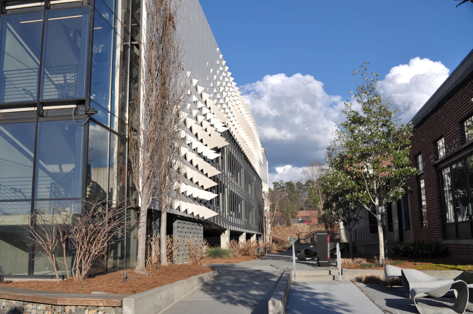 Modern urban street with contemporary buildings, trees, benches, and a clear sky with clouds.