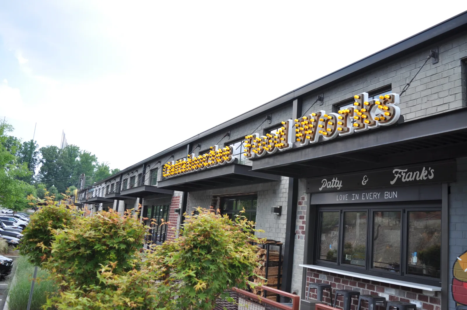 Exterior view of a brick food market with illuminated Food Works sign and greenery in front on a clear day