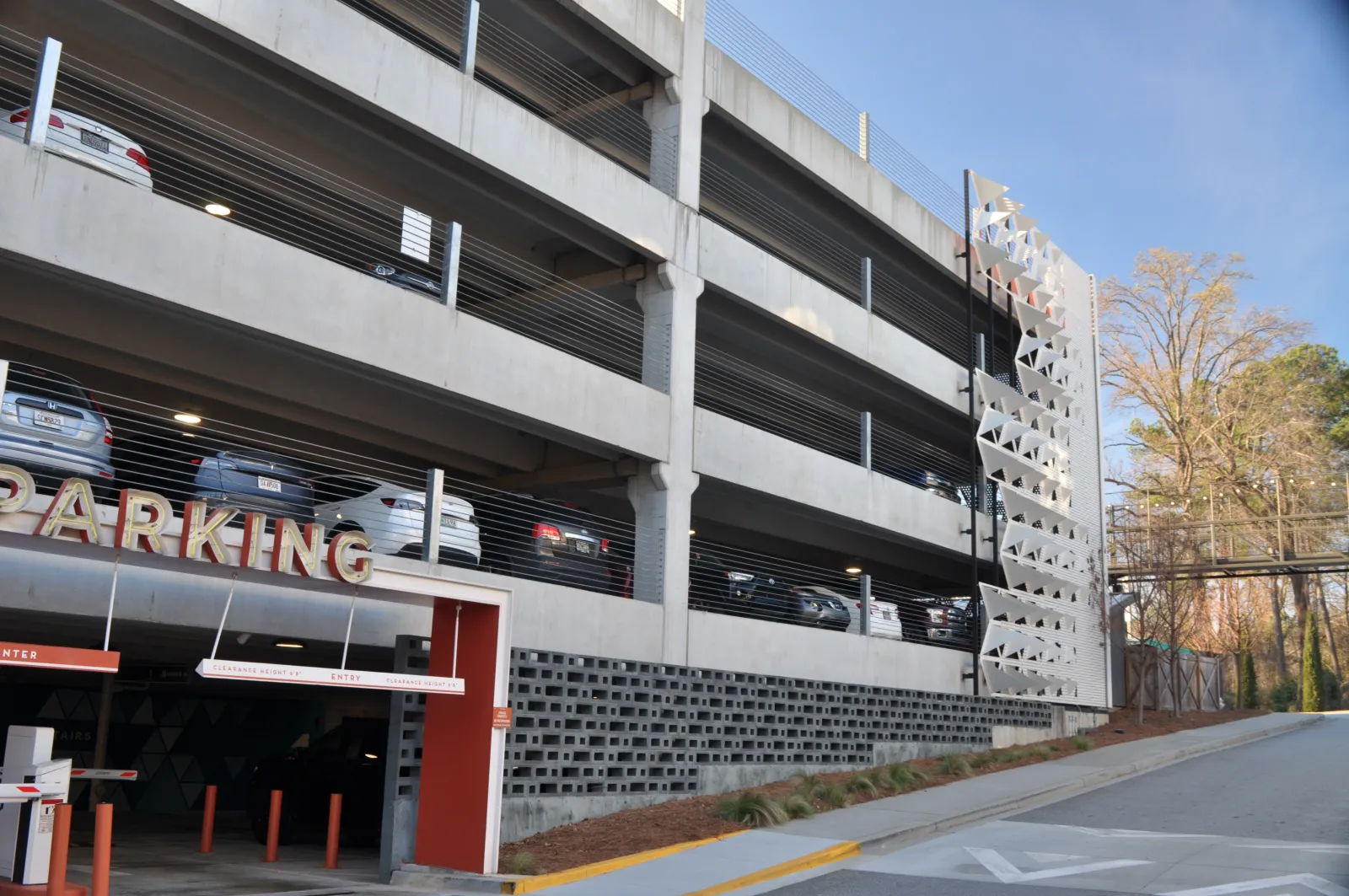 Multi-level concrete parking garage with cars parked inside and an entrance ramp on a sunny day.