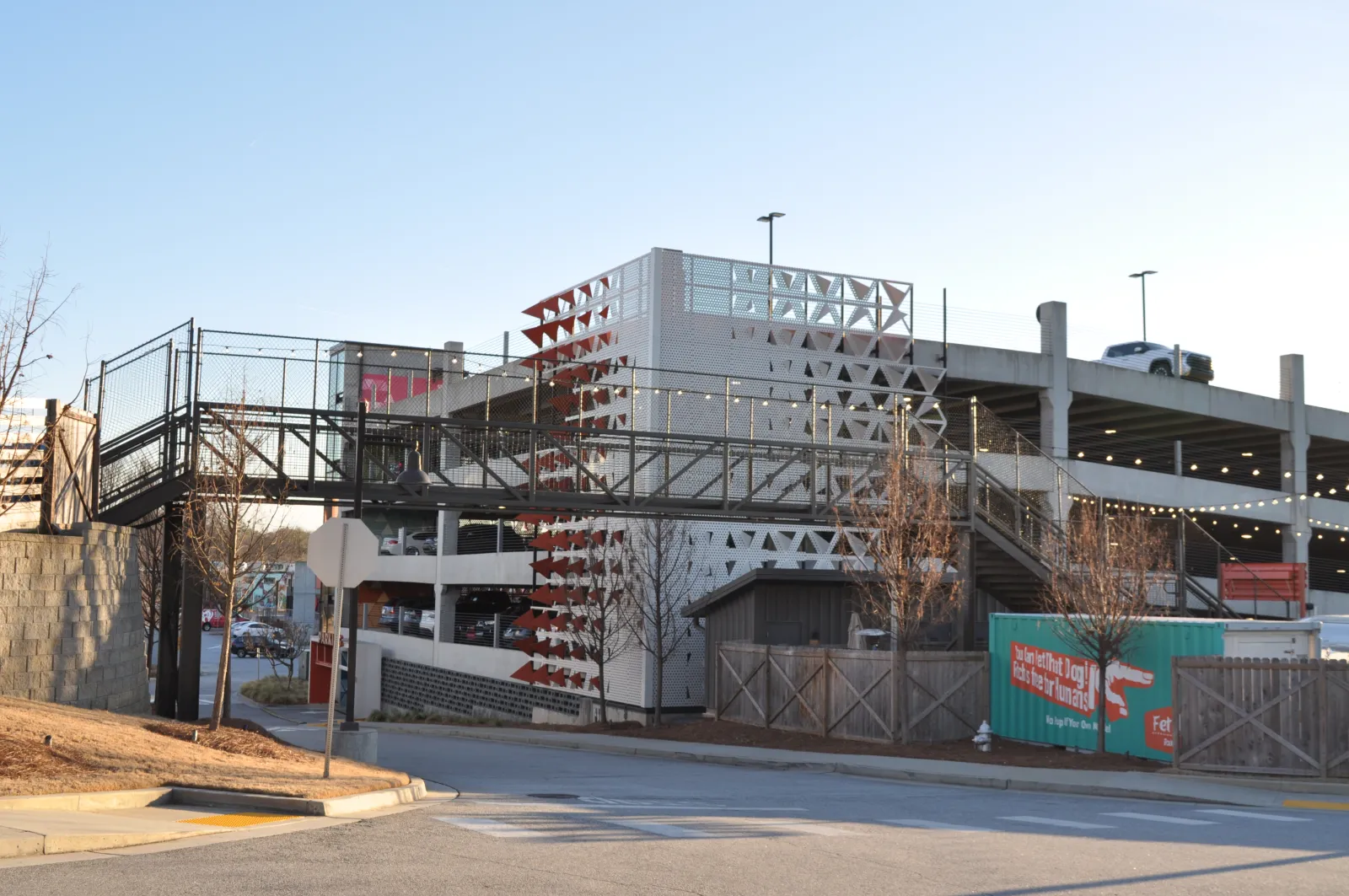 Modern multi-level parking garage with decorative panels and pedestrian bridge over street at sunset.