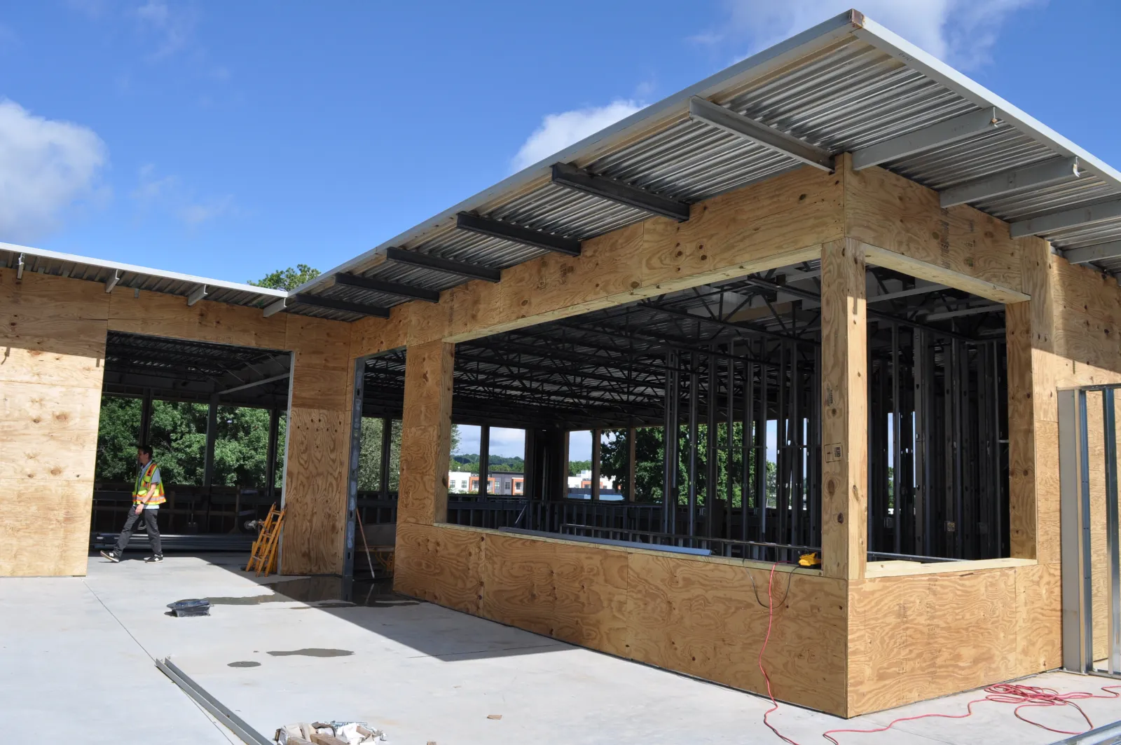 Construction site showing wood and metal framework of a building under clear blue sky with a worker in safety vest.