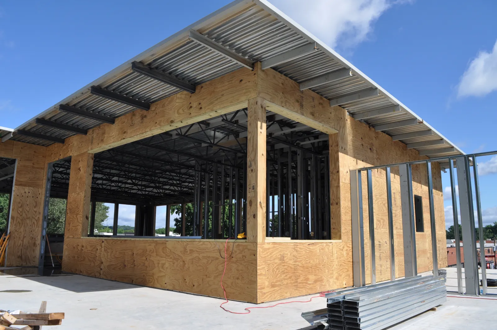 Construction site with wooden framing and metal beams under a clear blue sky, showing early building stages.