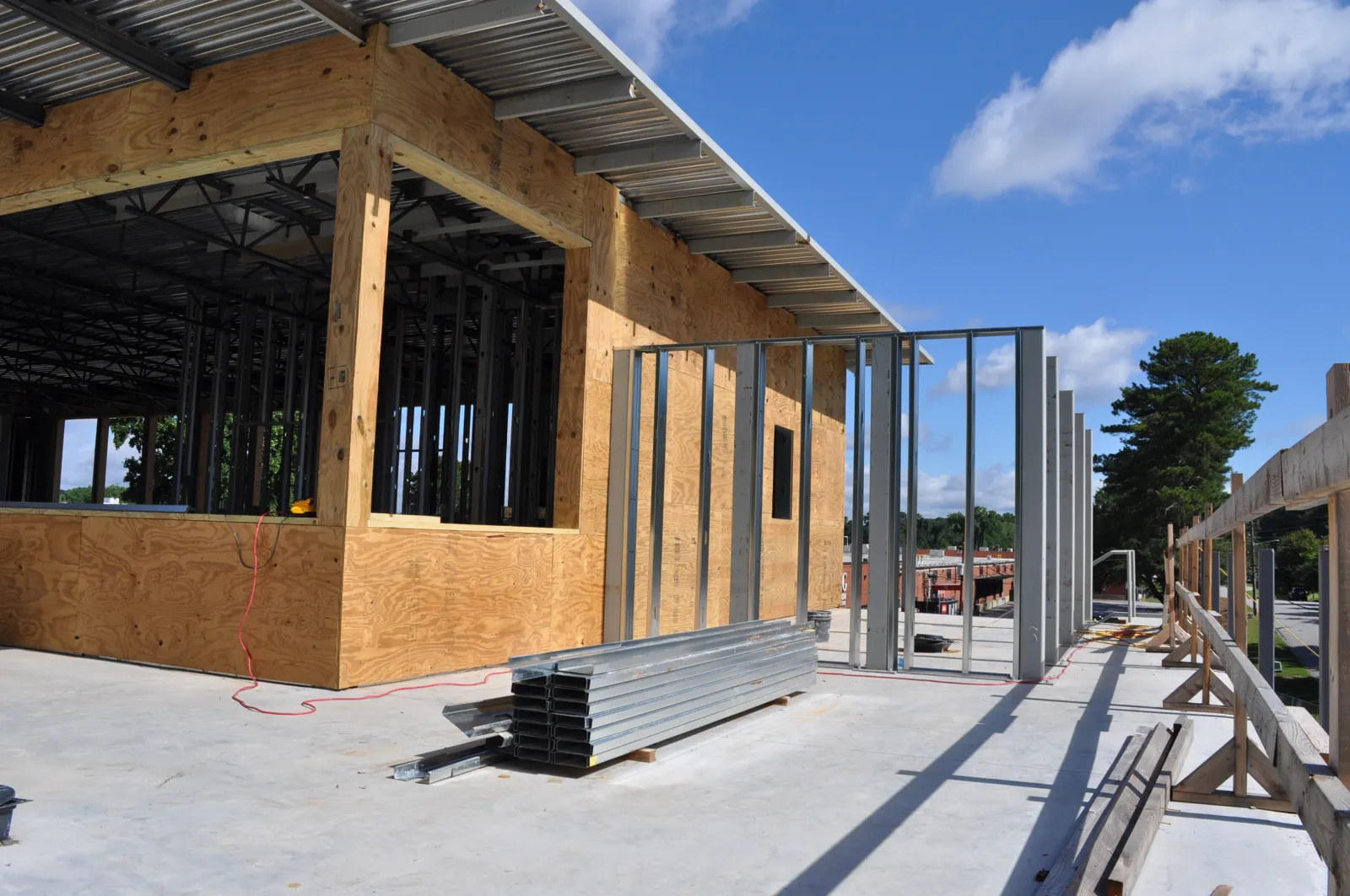 Construction site showing wooden framing and metal studs being installed under a clear blue sky.