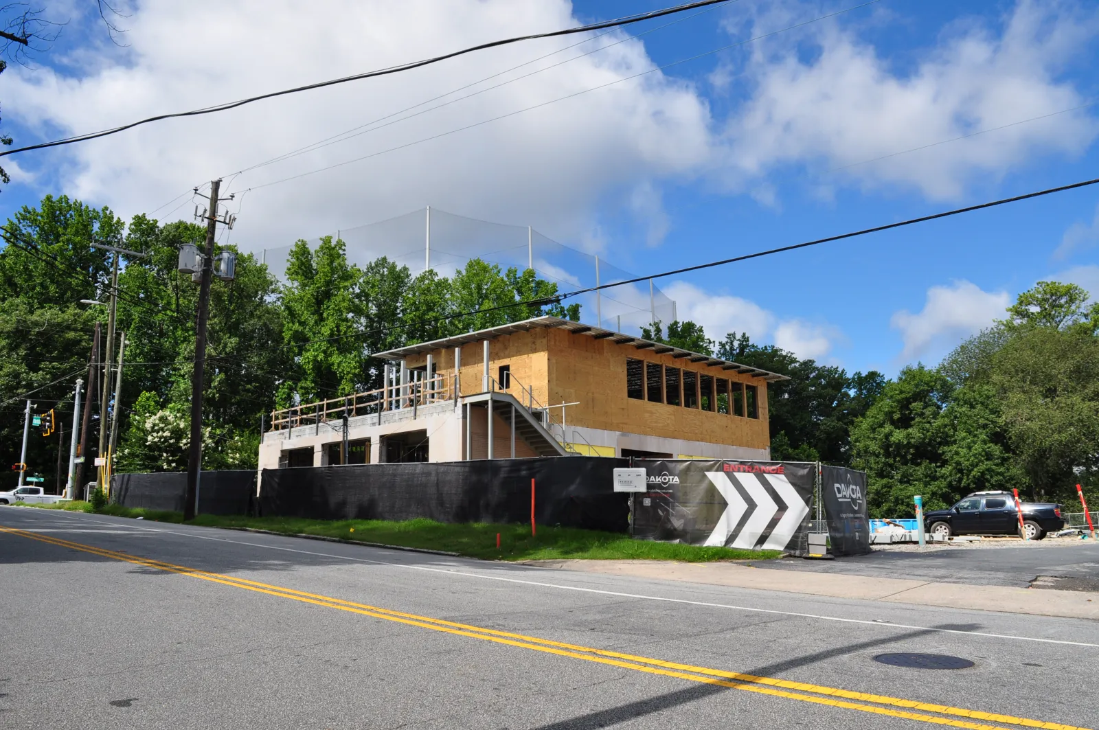Two-story building under construction with wooden framing, black fencing, and clear blue sky with clouds.
