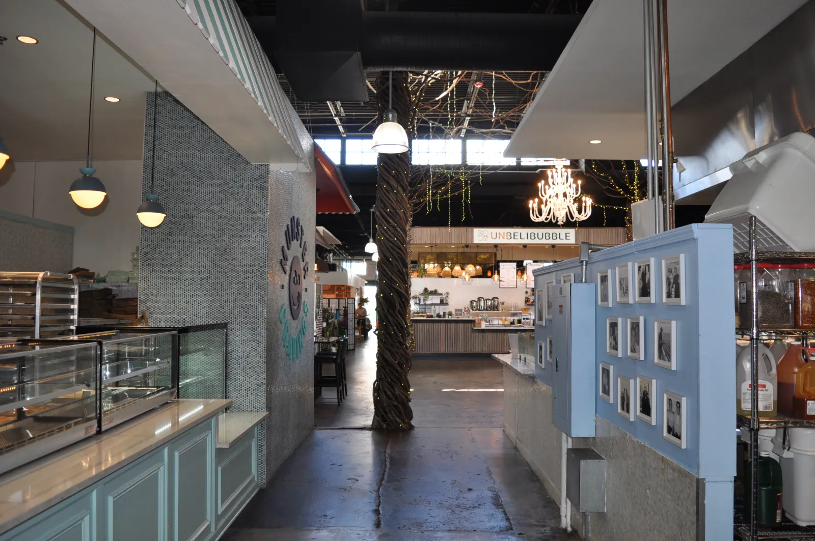 Interior view of a modern market with cafe counters, chandeliers, framed pictures, and decorative lights.