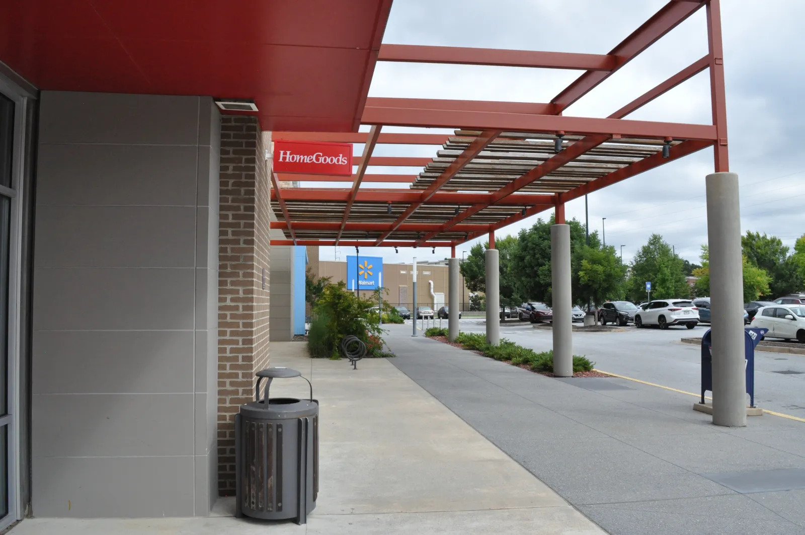 Outdoor shopping plaza with HomeGoods and Walmart stores under red metal canopy and parking lot on a cloudy day
