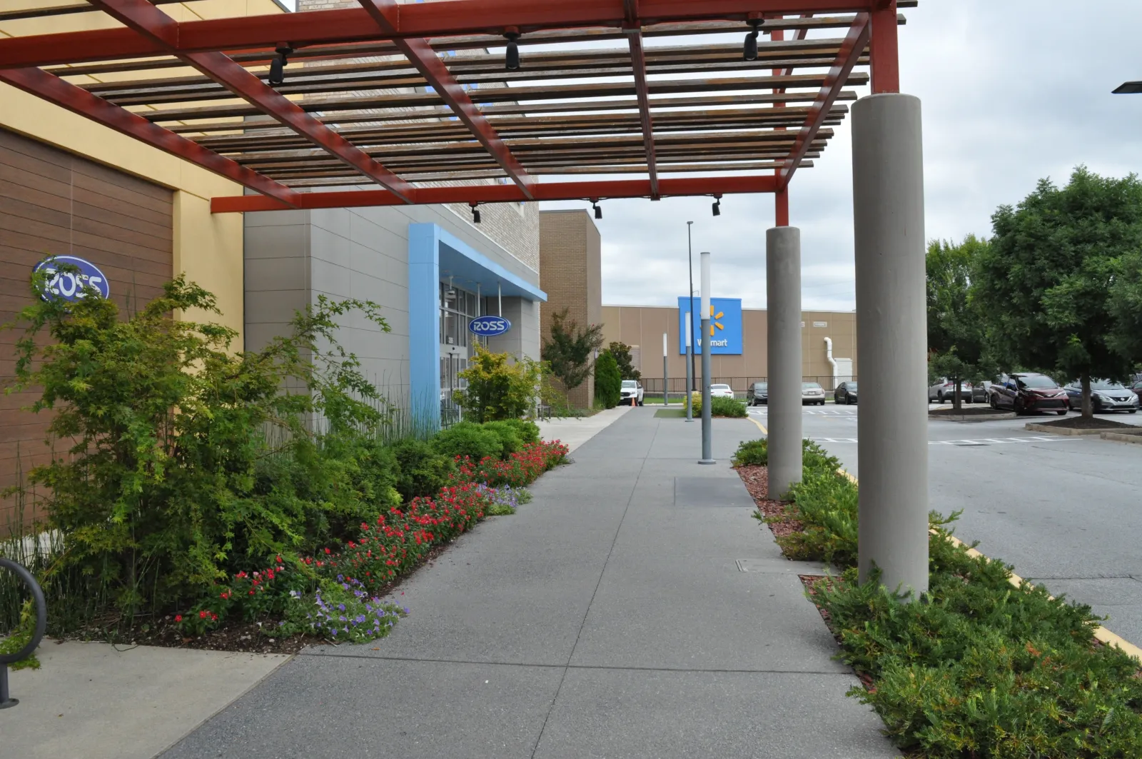 Outdoor shopping center walkway with Ross and Walmart stores, greenery, and covered pergola on a cloudy day.