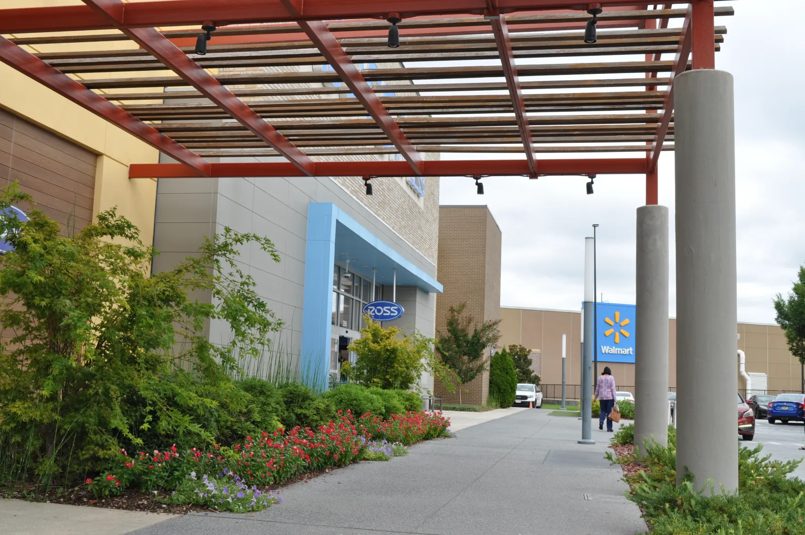 Outdoor walkway with modern pergola, landscaping, and store signs for Ross and Walmart on a cloudy day.
