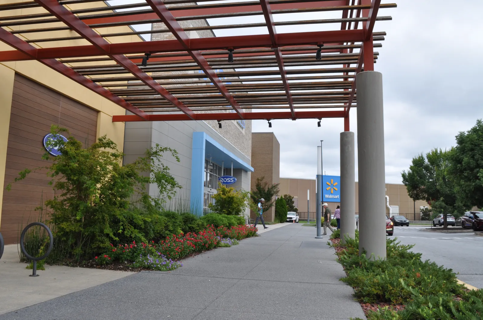 Outdoor walkway with a pergola, landscaped plants, and storefronts for Ross and Walmart in a shopping center.