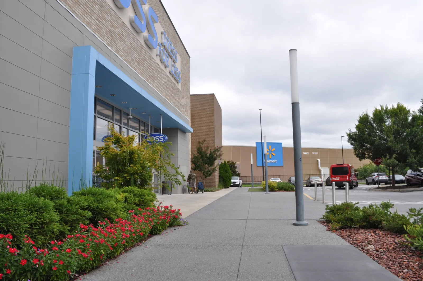 Outdoor view of a Ross Dress for Less store entrance with landscaping and a Walmart in the background under cloudy sky
