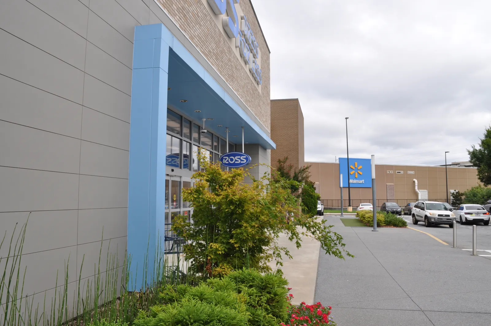 Exterior view of Ross store entrance with blue framing and Walmart building in the background under cloudy sky.