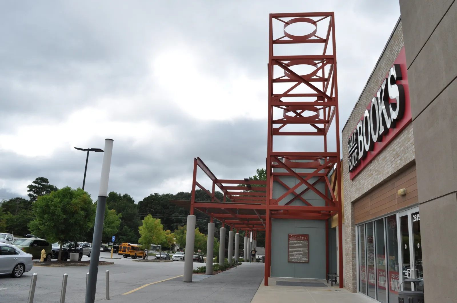 Exterior view of a bookstore with red metal framework and cloudy sky above a parking lot.