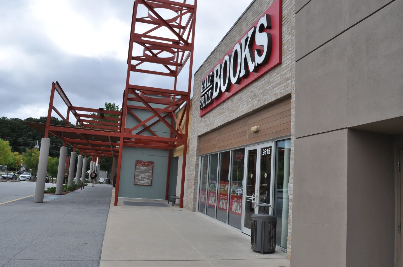 Exterior view of Half Price Books store with red metal framework and clear sidewalk under cloudy sky.