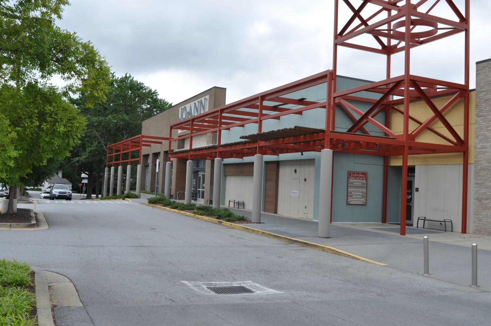 Exterior view of a Joann fabric and craft store with red metal awnings and a tree-lined parking area.