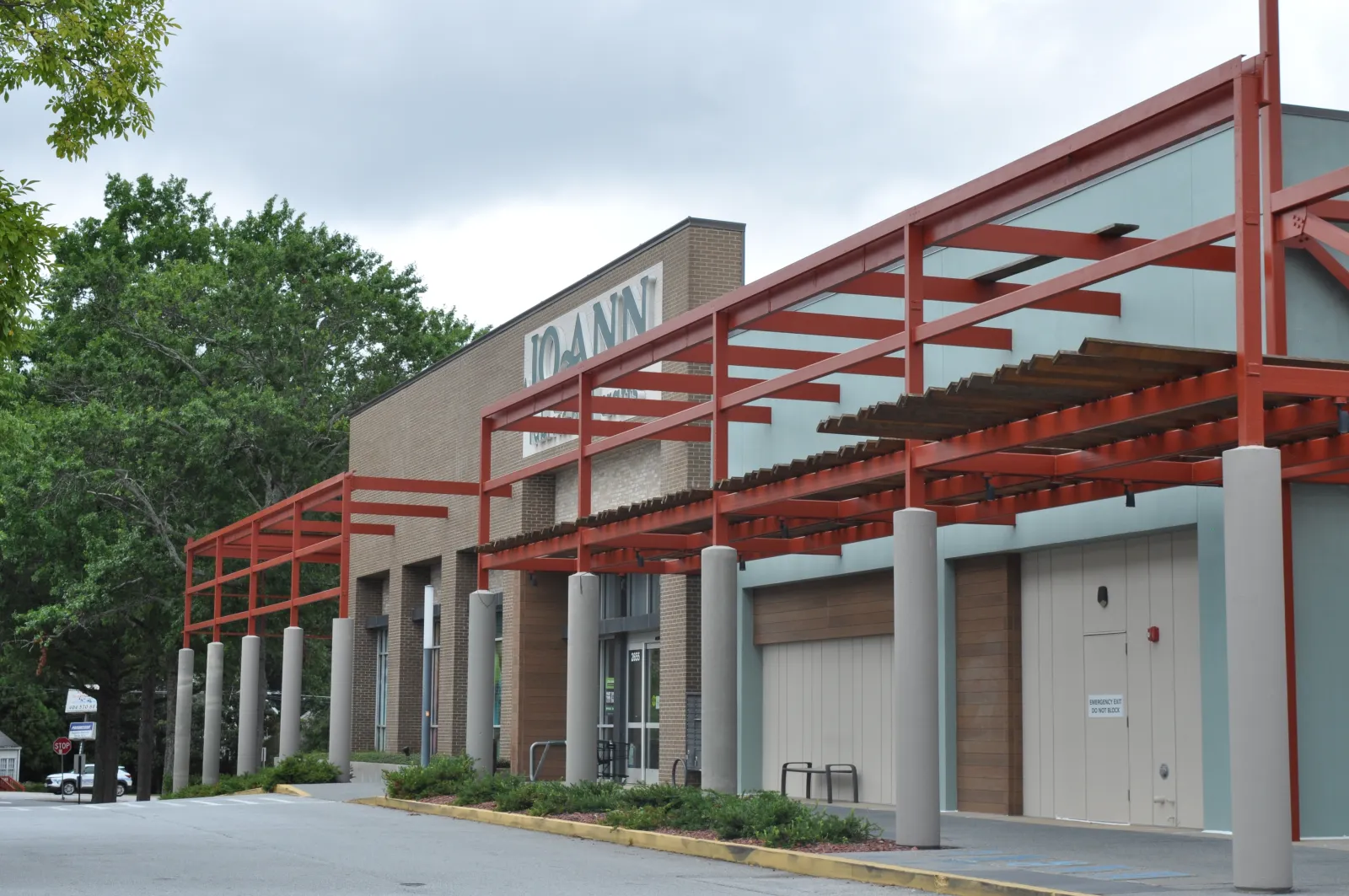 Exterior view of a Joann fabric and craft store with red metal framework and surrounding greenery